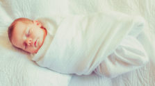 Swaddled infant asleep on a white background