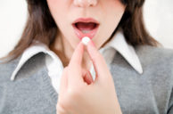 Close-up of young woman putting pill in mouth
